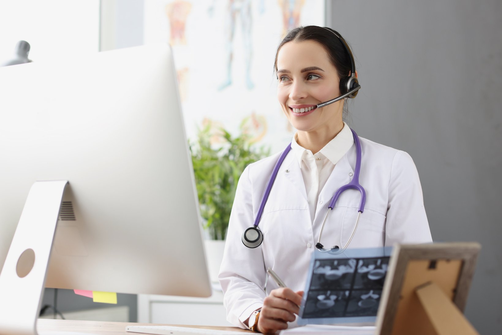 Doctor in Headphones with Microphone Holding X Ray in Front of Computer Screen